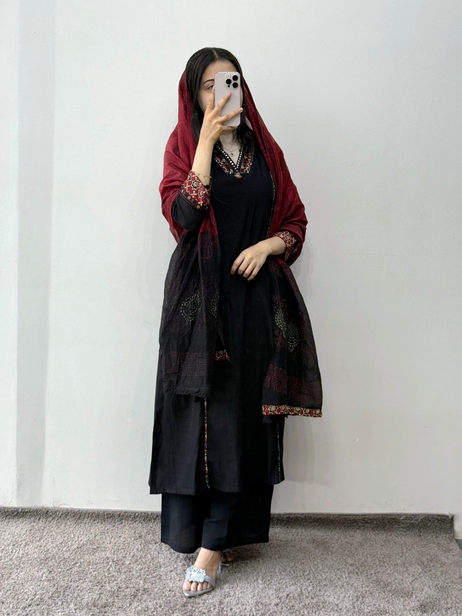 Woman wearing a black outfit with a red scarf against a white wall