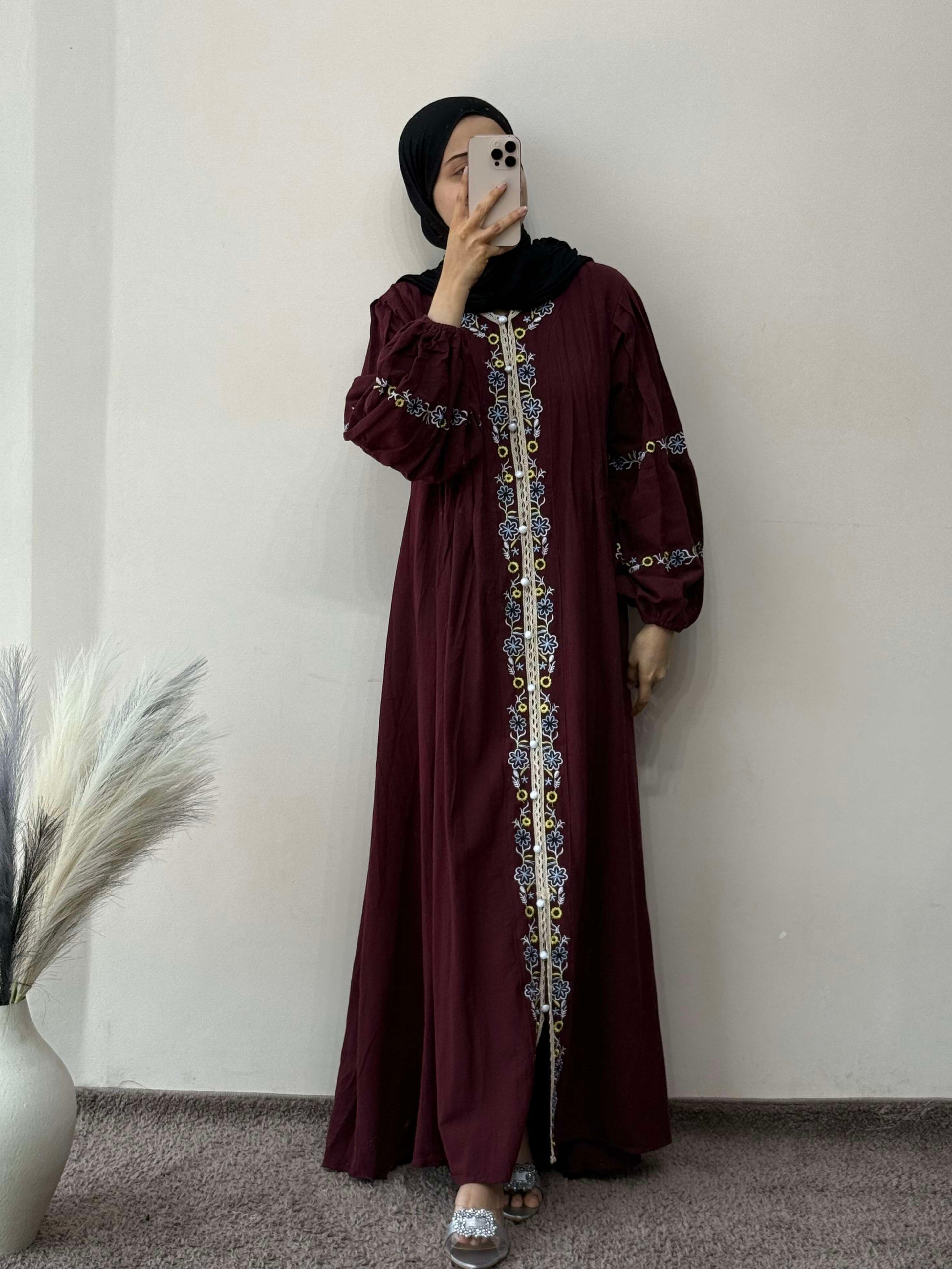 Person wearing a burgundy dress with intricate patterns, standing against a plain wall.
