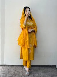 Person wearing a yellow traditional outfit with a matching dupatta against a white wall.
