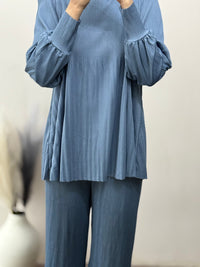 Person wearing a blue ribbed sweater and matching pants against a neutral background