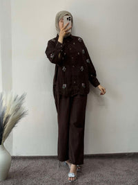 Person wearing a dark brown outfit with floral patterns against a plain wall.