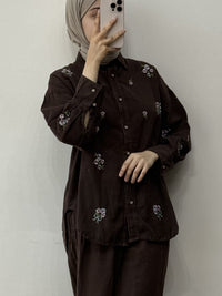 Person wearing a dark brown outfit with floral embroidery against a plain background