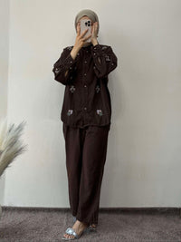 Person wearing a brown outfit with floral embroidery in a minimal indoor setting.