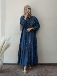 Person wearing a blue denim dress standing against a plain wall.
