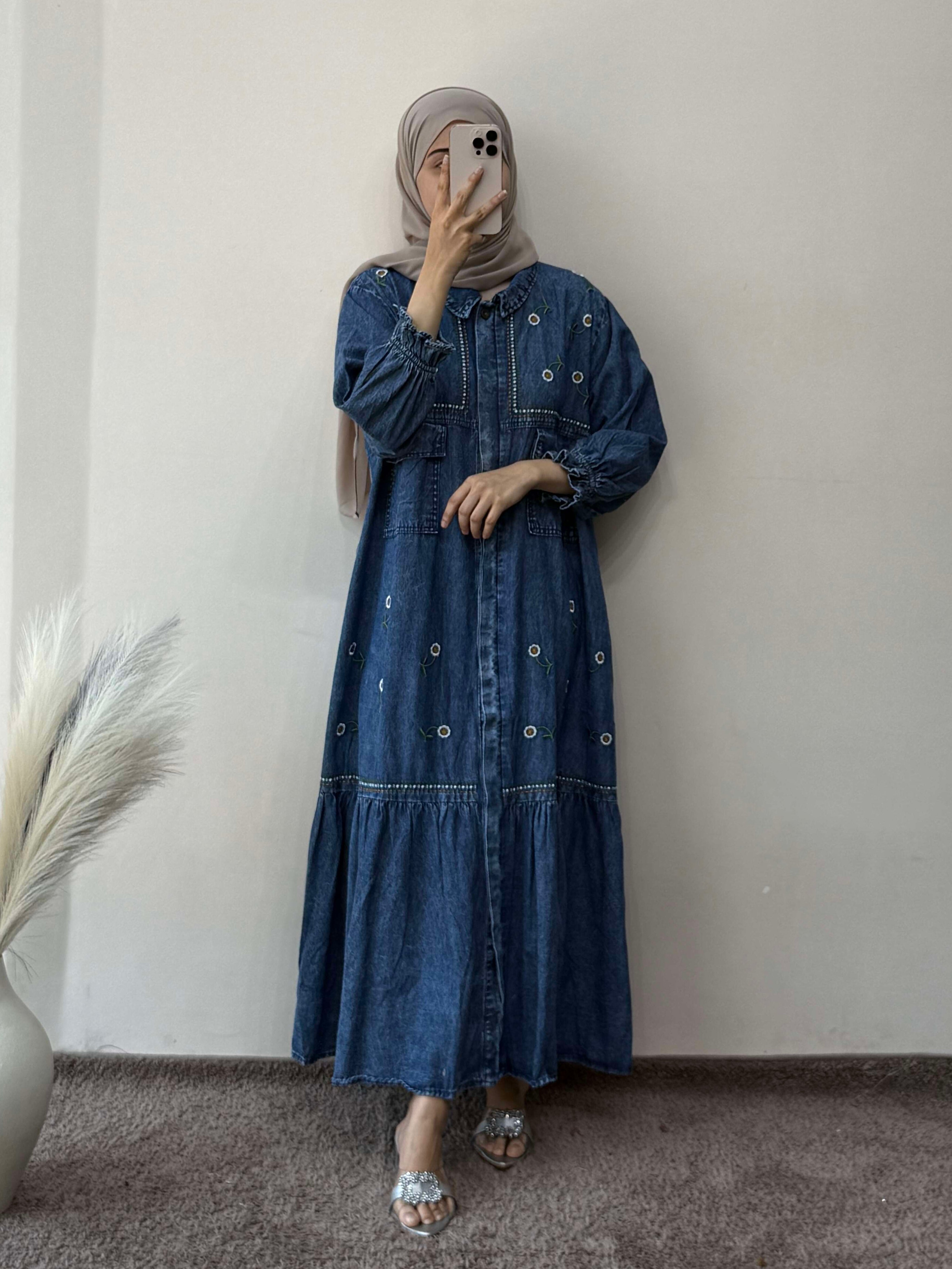 Person wearing a blue denim dress standing against a plain wall.