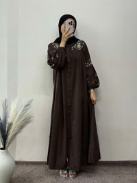 Person wearing a long brown dress with floral embroidery against a plain background