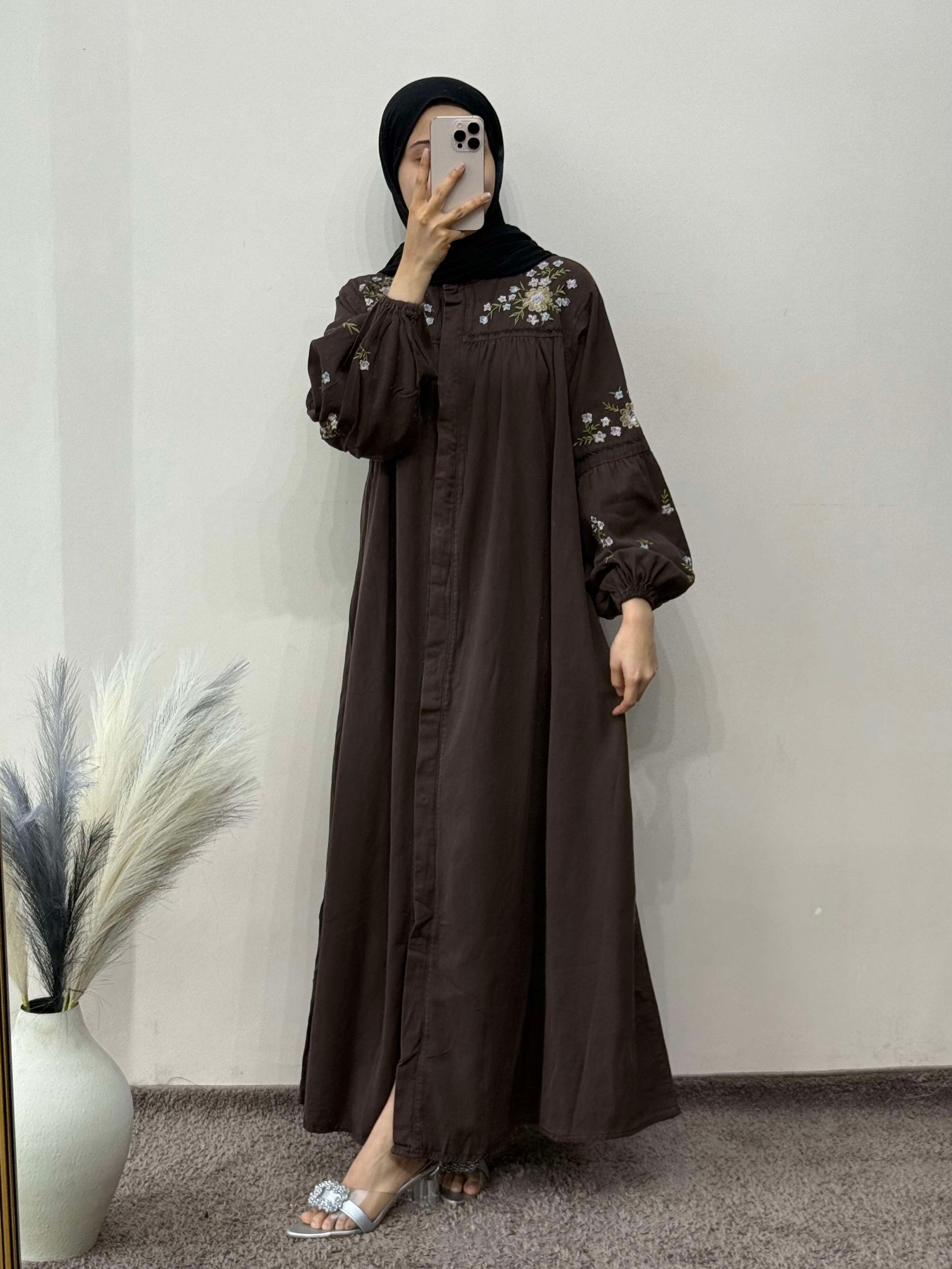 Person wearing a brown dress with floral embroidery in a minimal indoor setting.