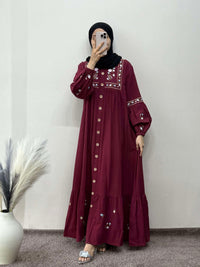 Person wearing a burgundy dress with intricate embroidery in a minimal indoor setting.