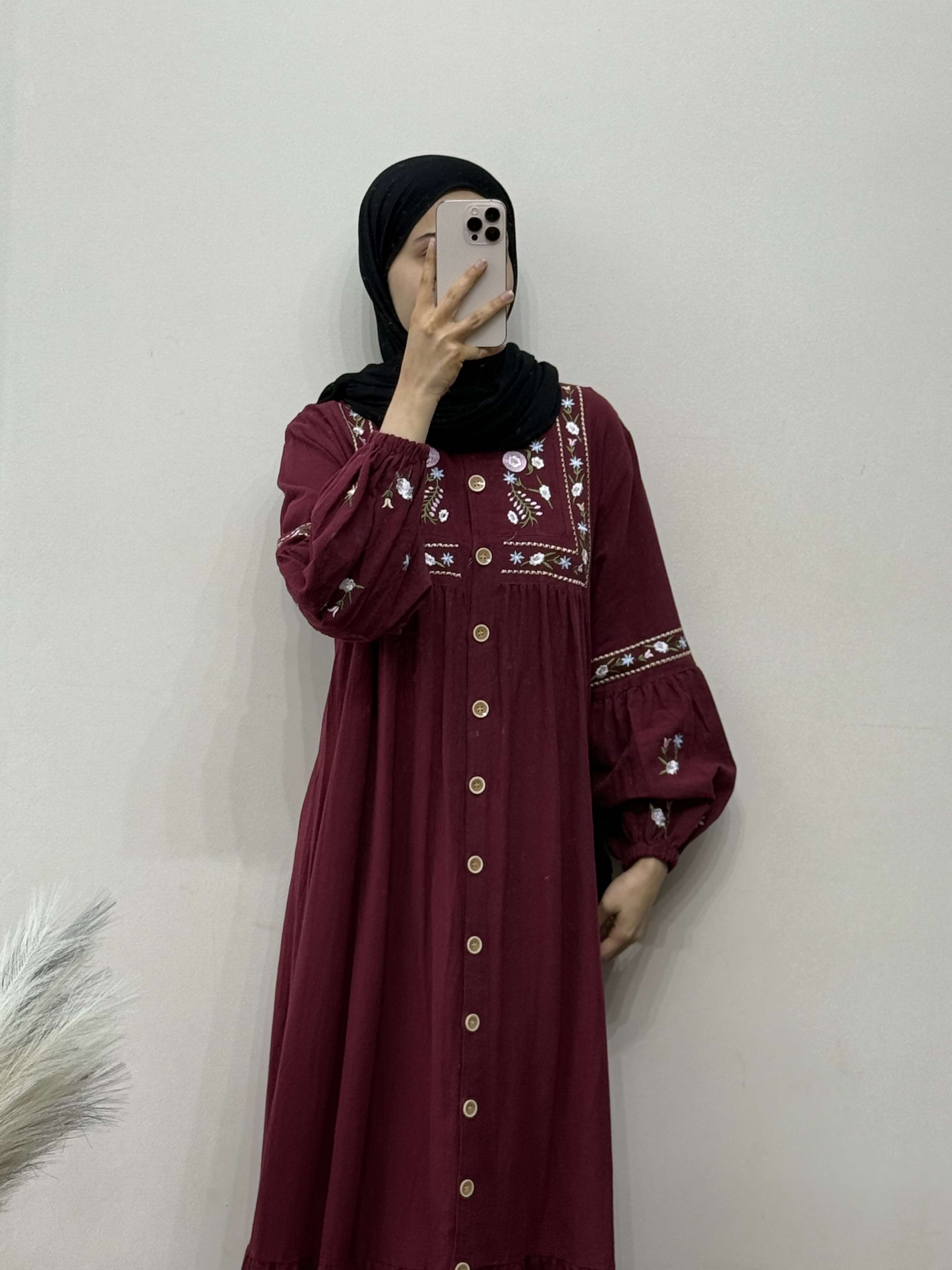 Person wearing a burgundy dress with intricate patterns against a plain background