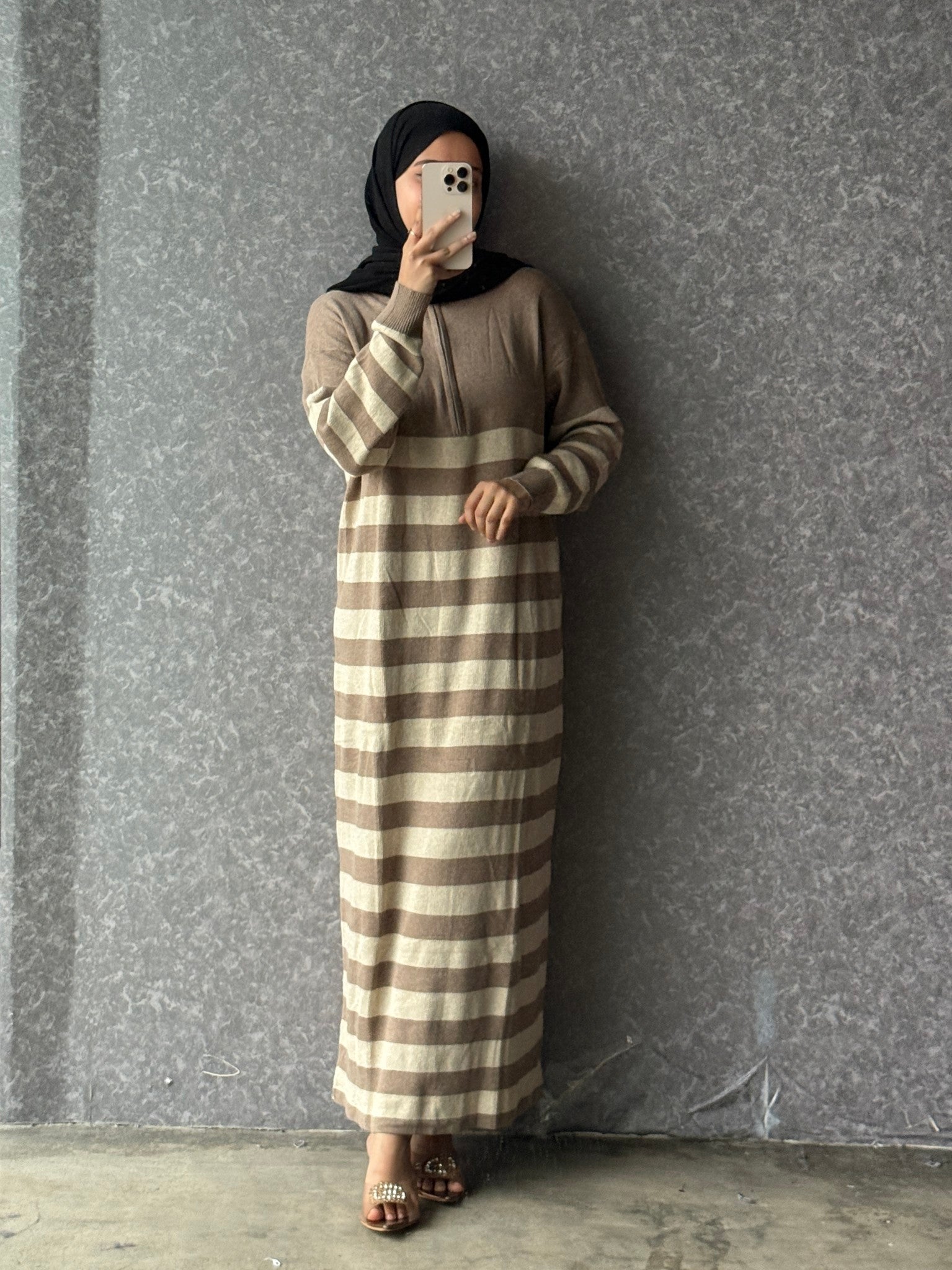 Person wearing a brown and beige striped dress against a gray wall.