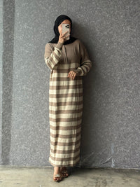 Person wearing a brown and beige striped dress against a gray wall.