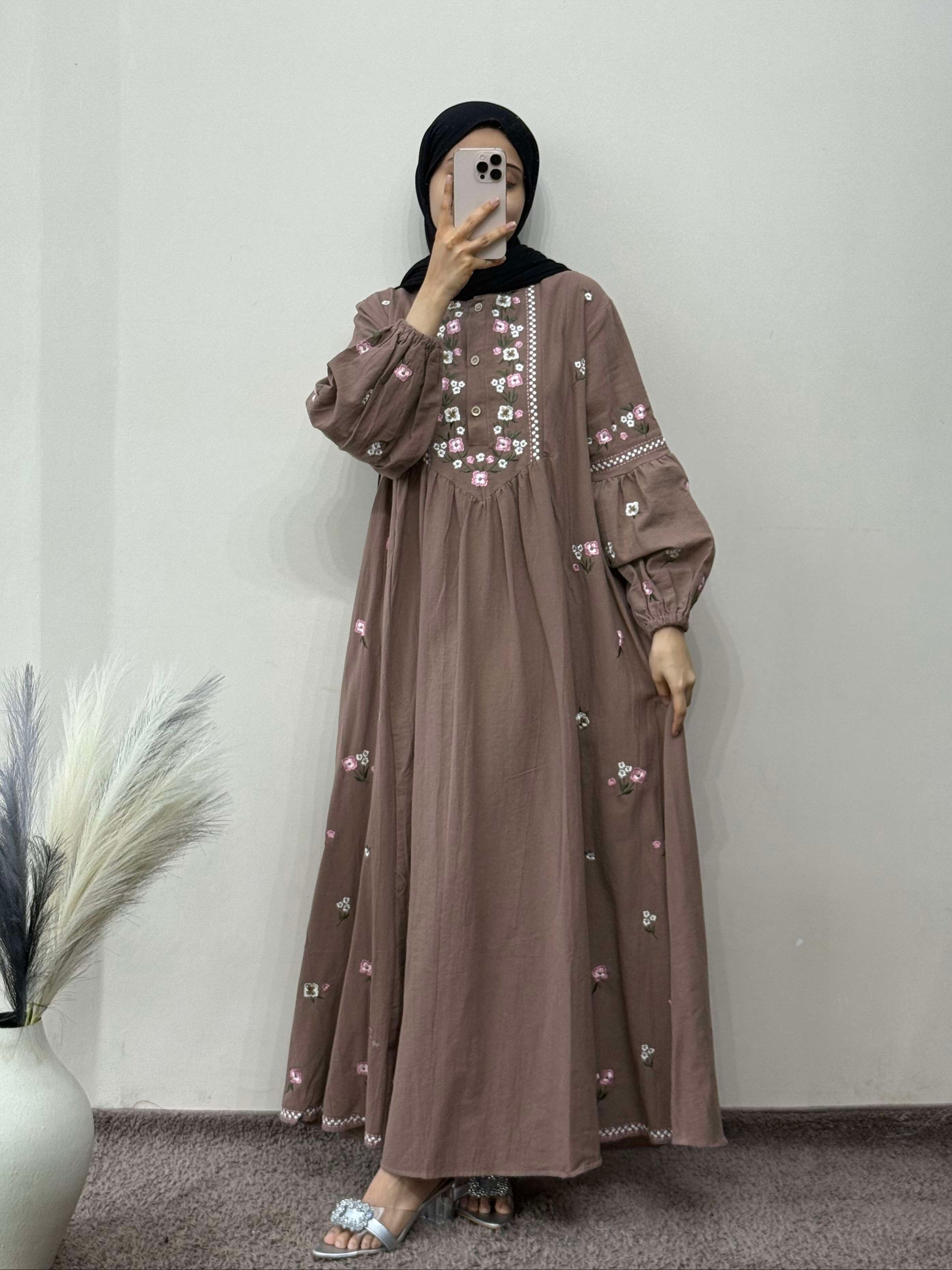 Person wearing a brown dress with floral embroidery against a plain background