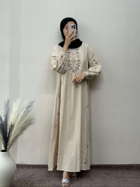 Person wearing a long beige dress with floral patterns against a plain wall.