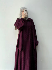 Person wearing a burgundy dress with a matching hijab against a white background