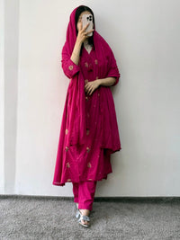 Person wearing a magenta traditional outfit with a matching dupatta against a white wall.