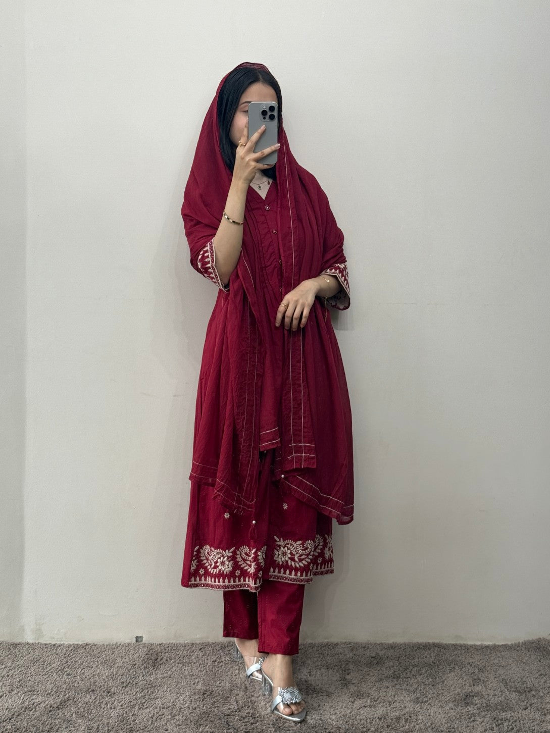 Person wearing a maroon traditional outfit with white patterns against a plain background