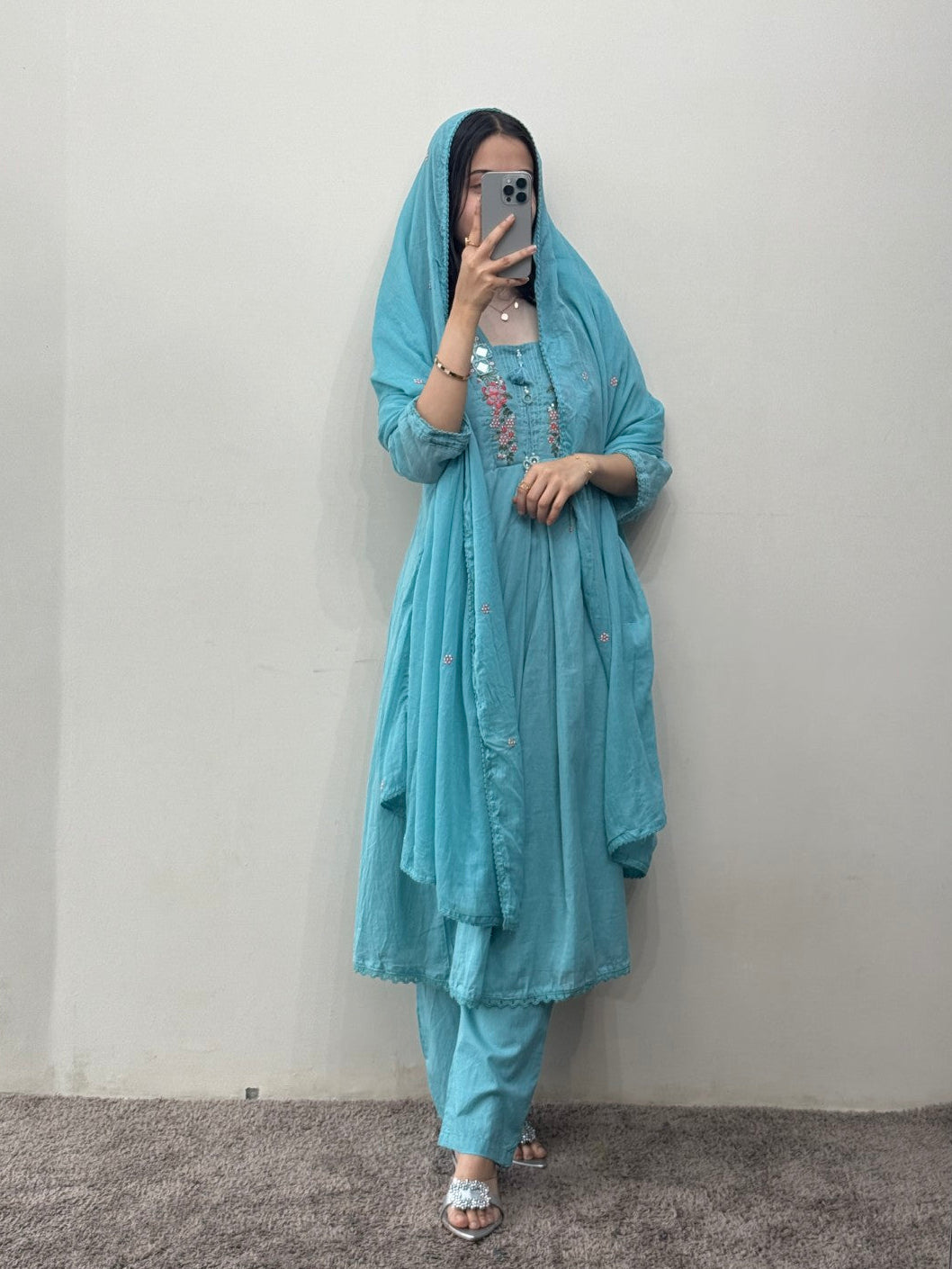 Person wearing a light blue traditional outfit with a matching headscarf against a plain background.