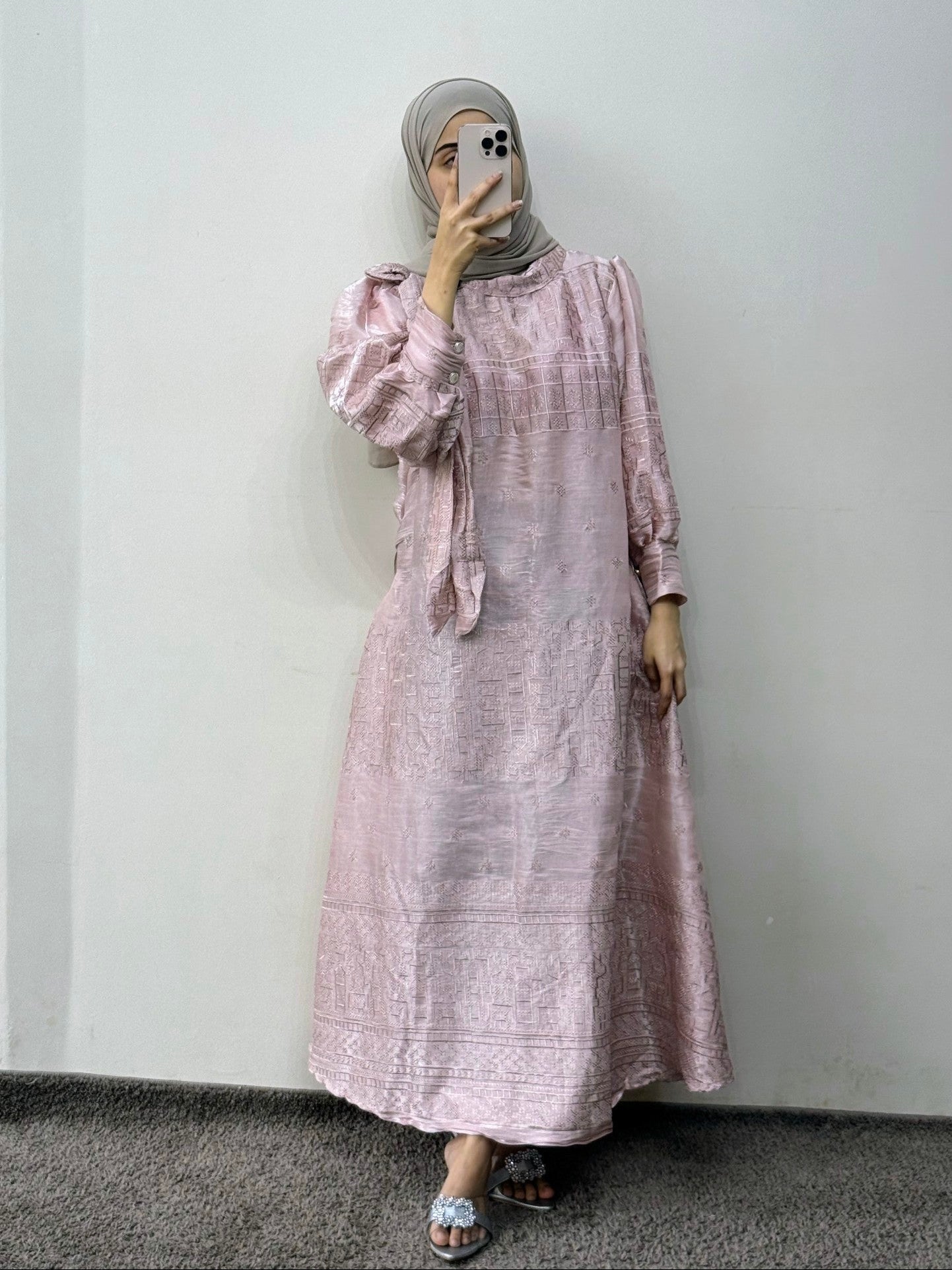 Person wearing a pink dress with long sleeves and a matching headscarf against a plain background
