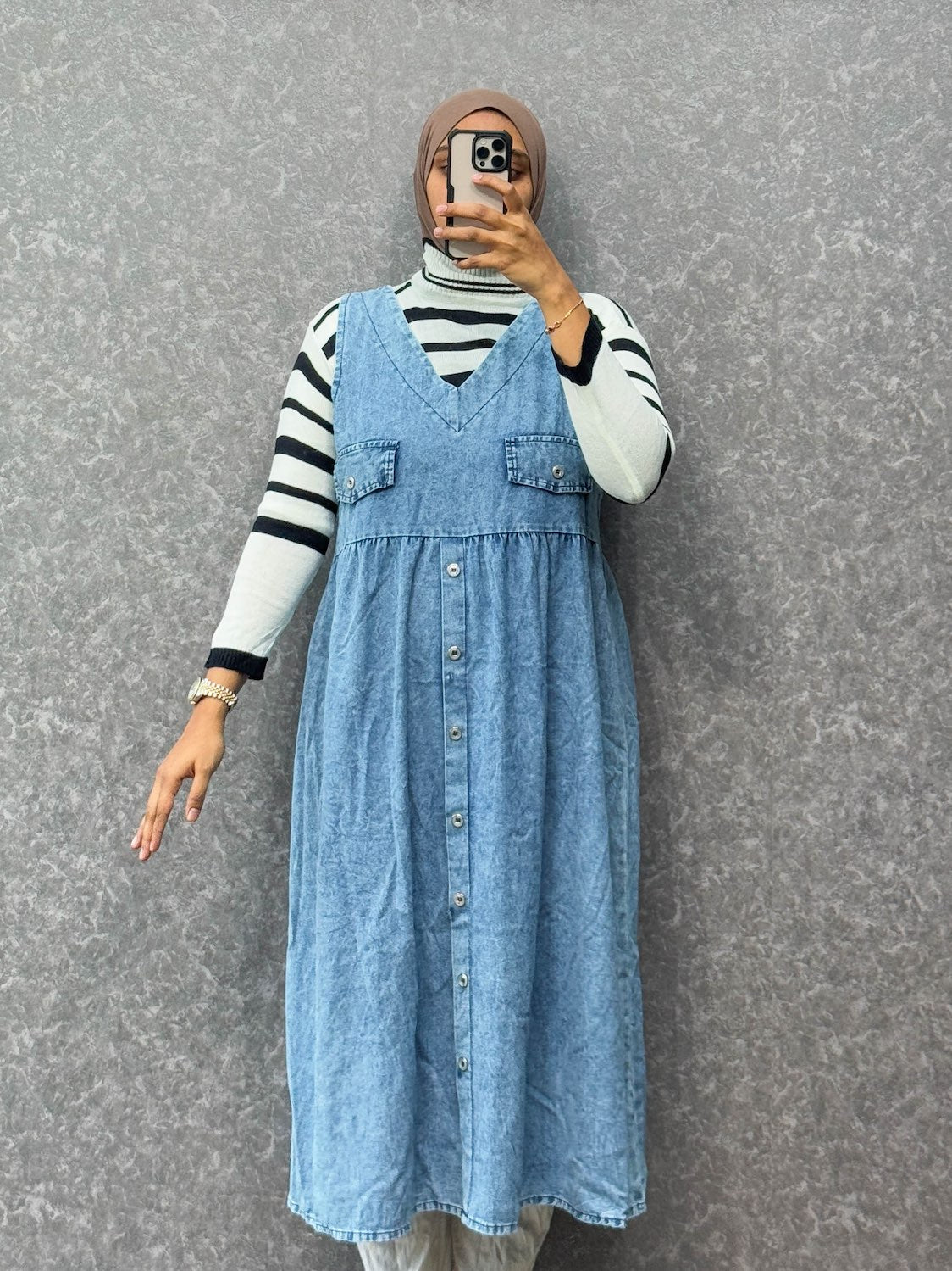 Person wearing a blue denim dress over a striped shirt against a gray background