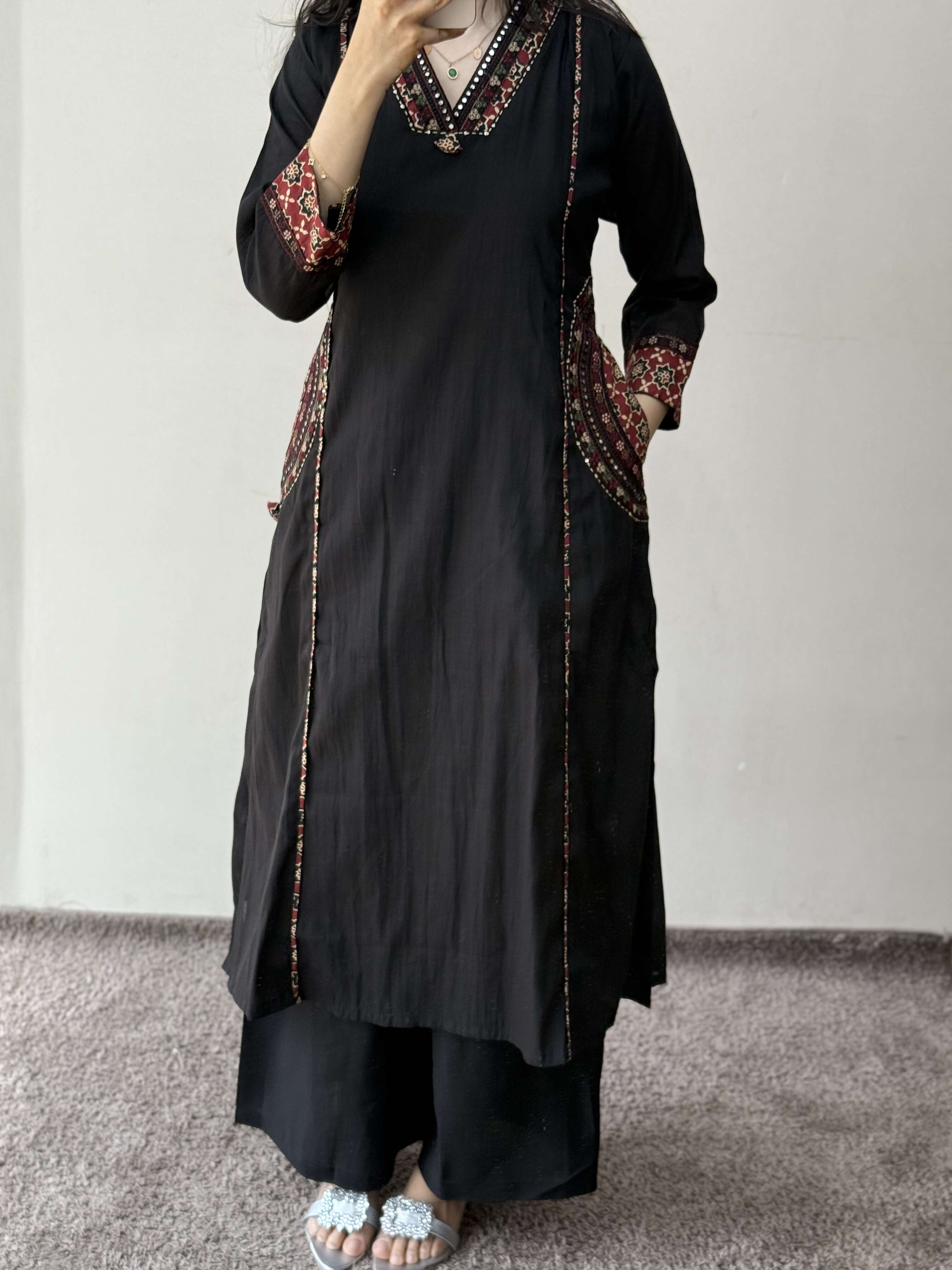 Person wearing a black outfit with patterned details on a plain background