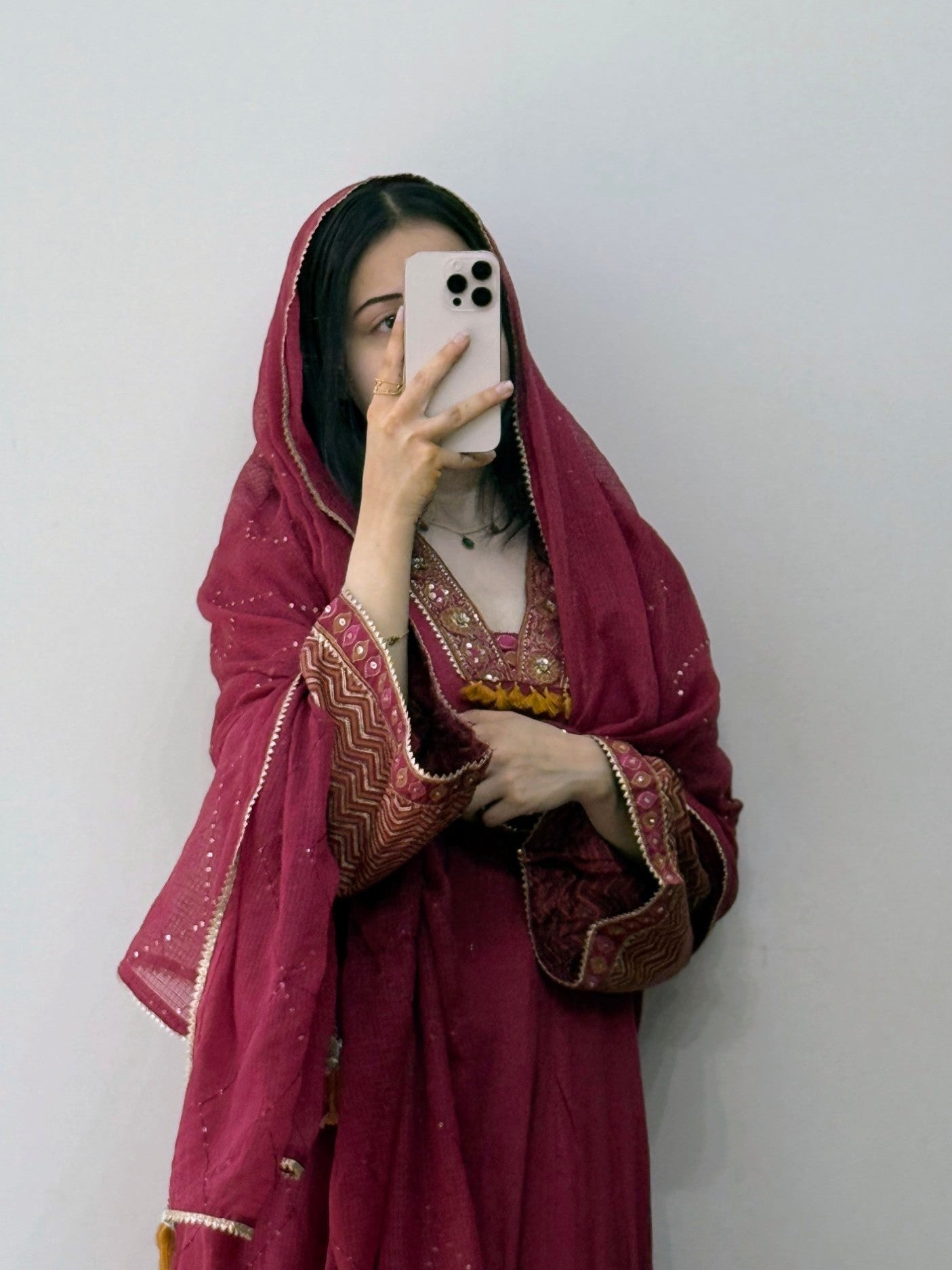 Person wearing a traditional maroon outfit with intricate patterns, holding a phone.