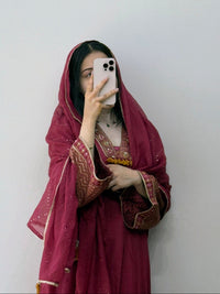 Person wearing a traditional maroon outfit with intricate patterns, holding a phone.
