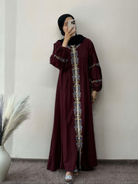 Person wearing a burgundy dress with intricate patterns, standing against a plain wall.