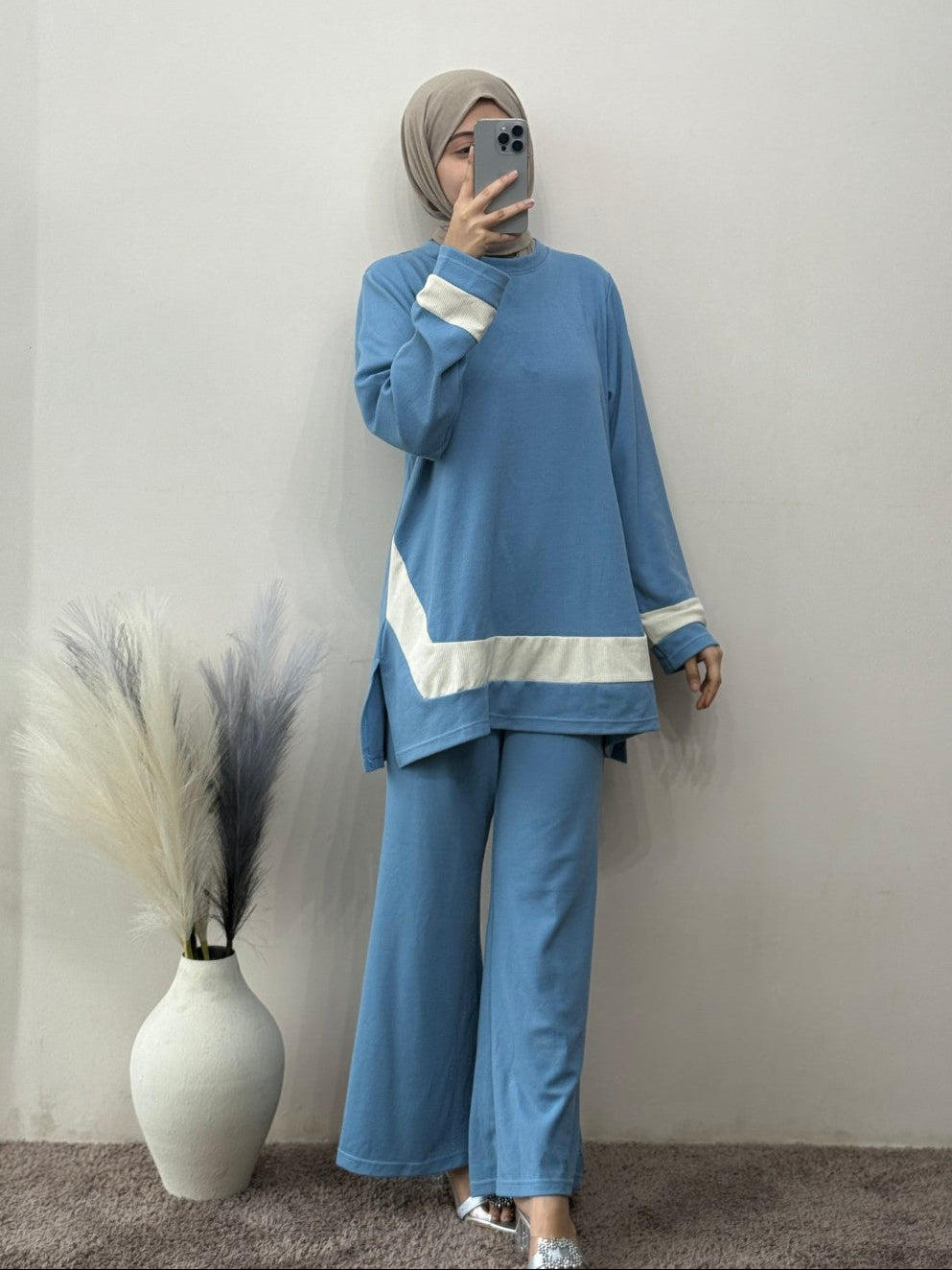 Person wearing a blue outfit with white accents standing against a plain wall.