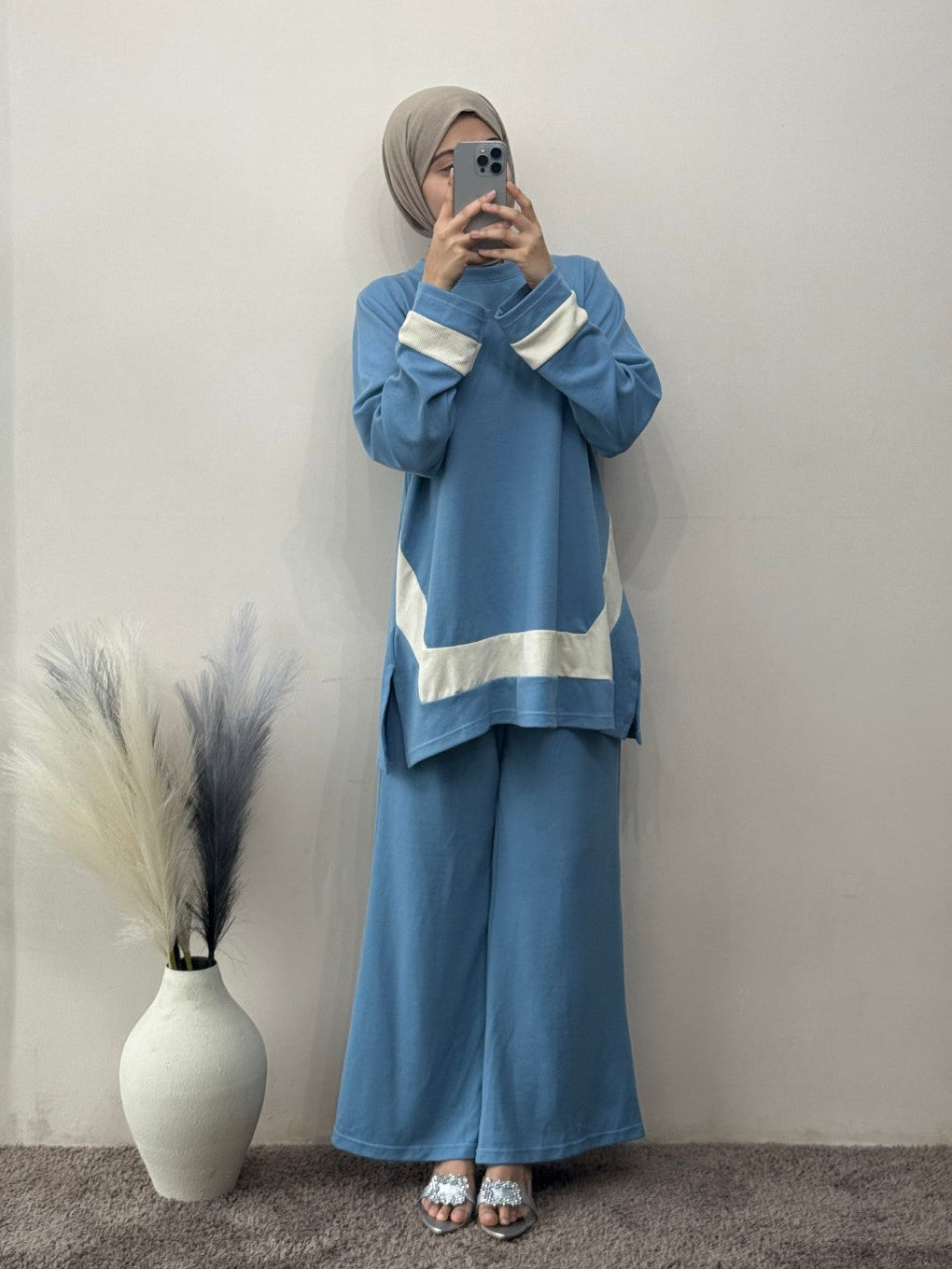 Person wearing a blue outfit with white stripes standing against a plain wall.