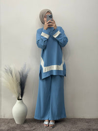 Person wearing a blue outfit with white stripes standing against a plain wall.