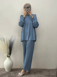 Person wearing a blue outfit taking a mirror selfie against a plain wall.