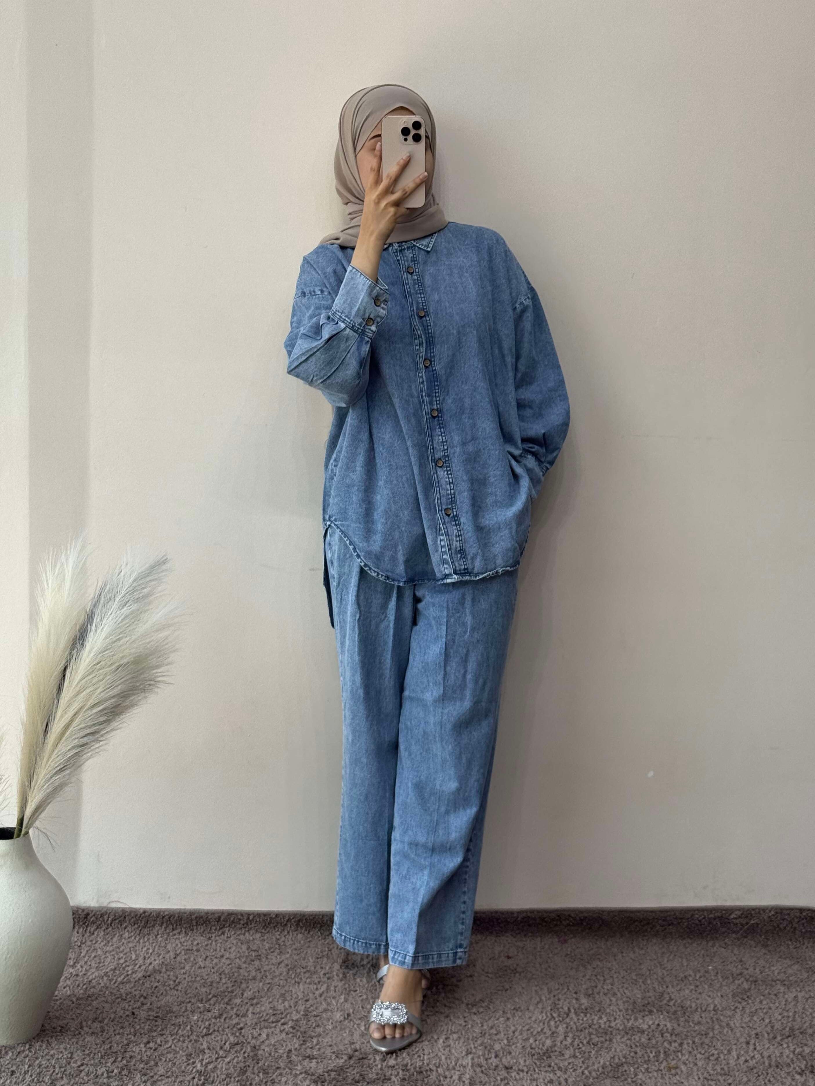 Person wearing a denim outfit standing against a plain wall.