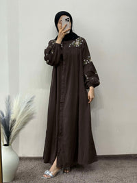 Person wearing a brown dress with floral embroidery in a minimal indoor setting.