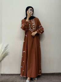 Person wearing a brown dress with white patterns against a plain wall.