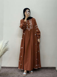 Person wearing a brown dress with white patterns in a room.