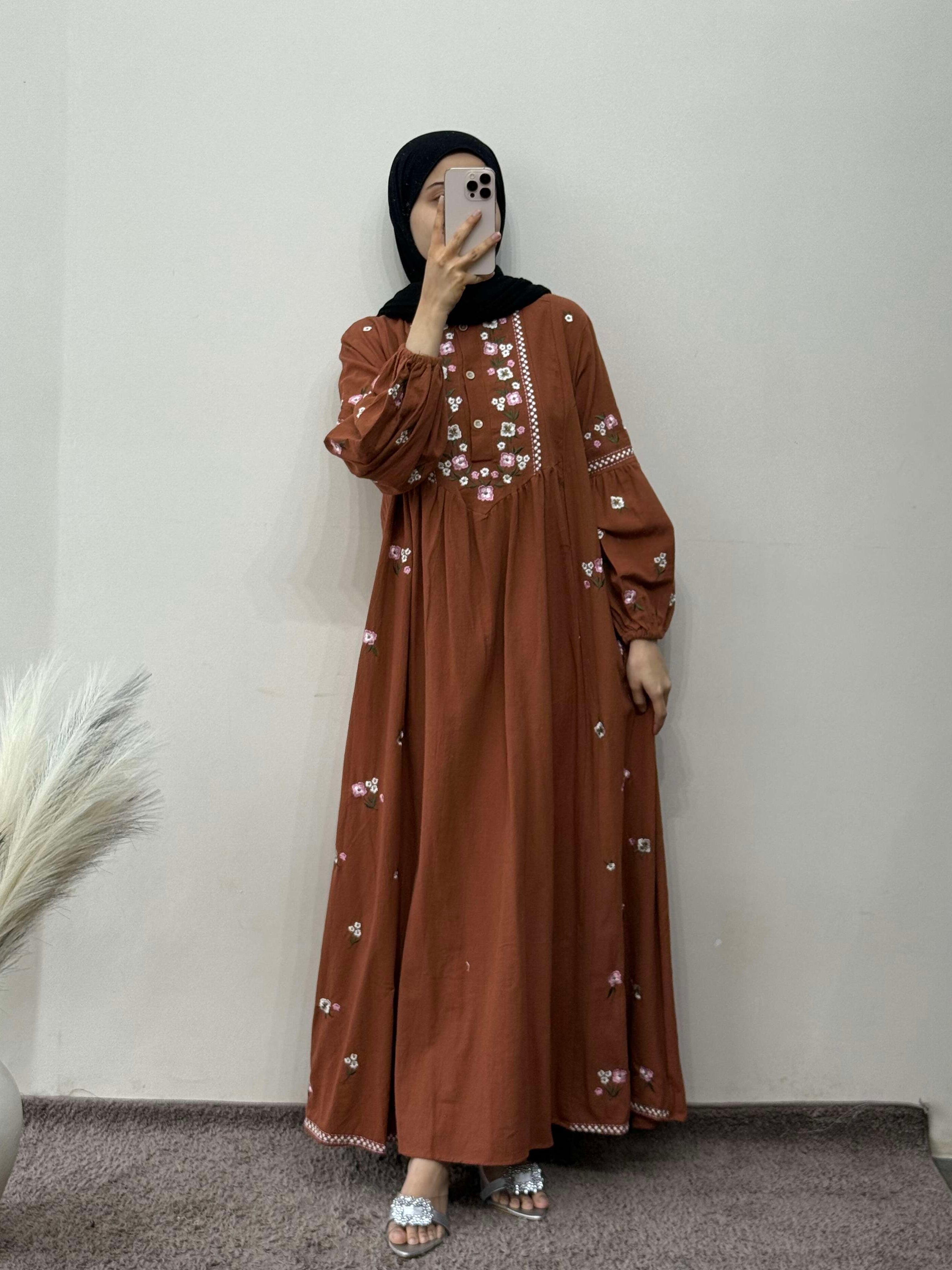 Person wearing a brown dress with white patterns in a room.