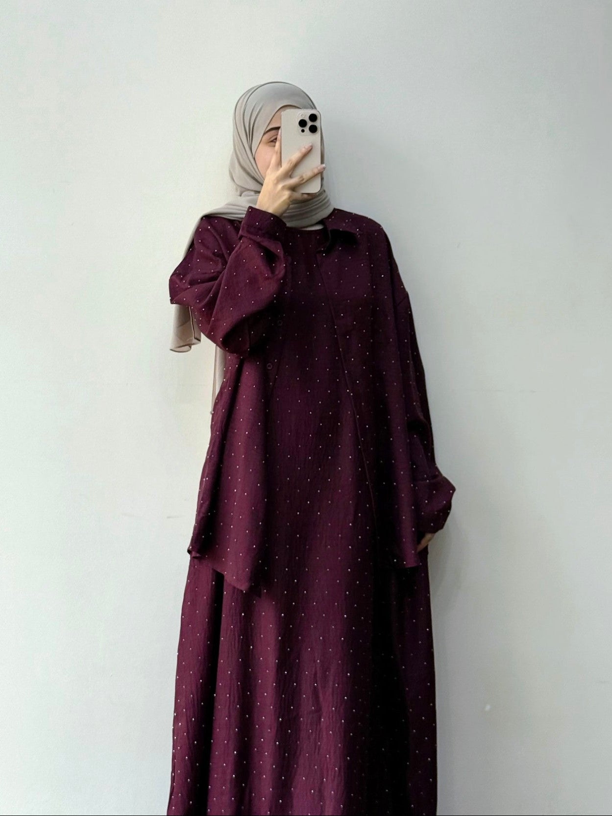 Person wearing a burgundy dress with a matching hijab against a white background