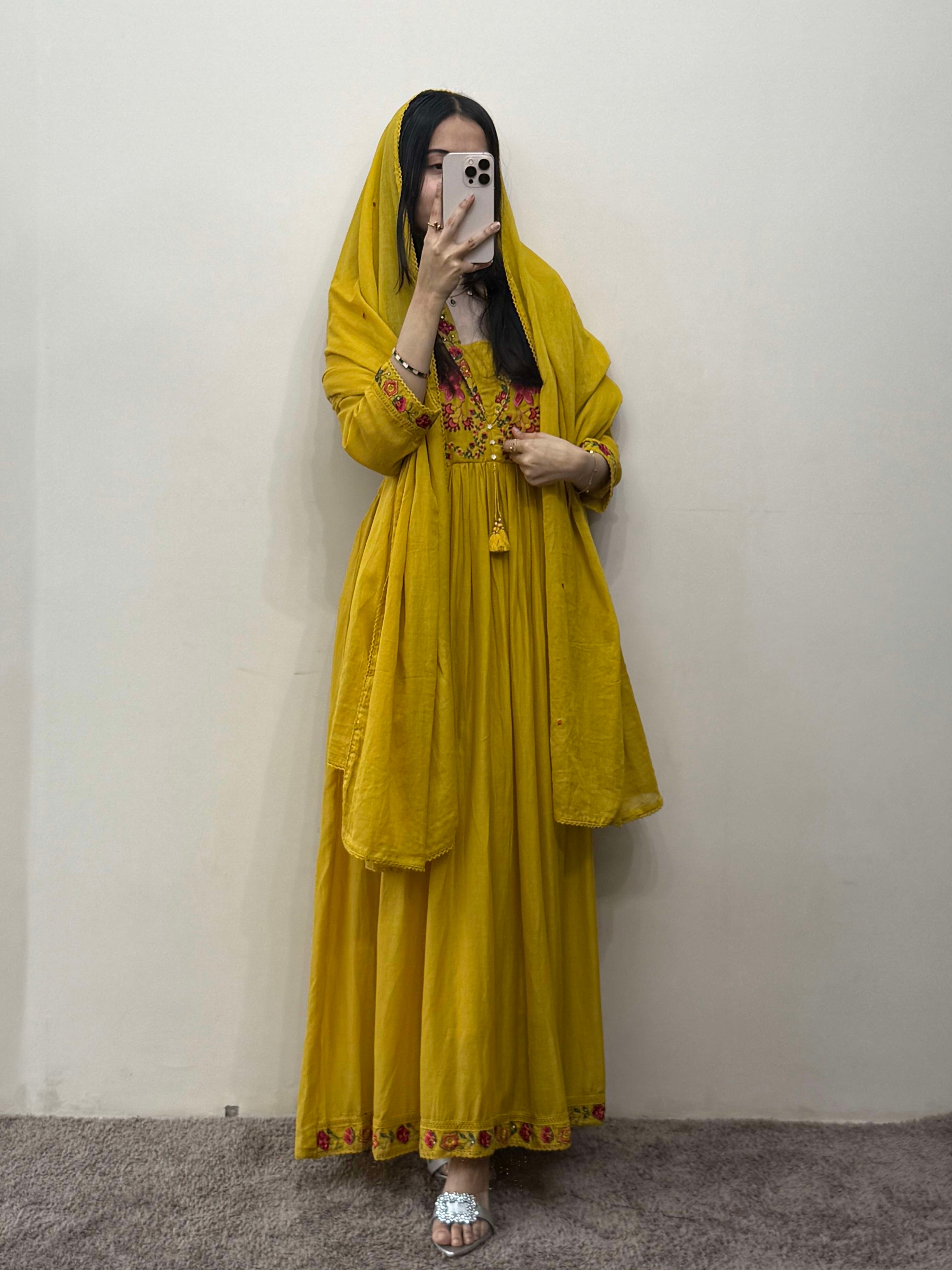 Person wearing a yellow traditional outfit with a matching headscarf in front of a plain wall.