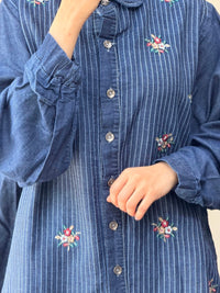 Blue striped shirt with floral embroidery on a plain background