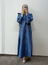 Person wearing a blue dress with ruffled sleeves against a white wall.