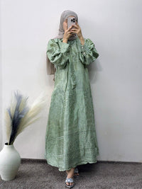 Person wearing a green dress with puff sleeves in front of a white wall.