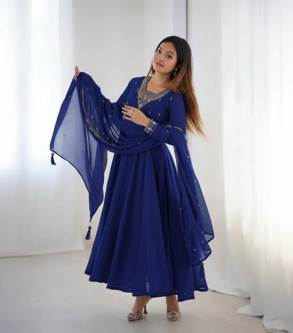 Woman in a blue traditional outfit with a matching dupatta against a white curtain background