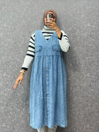 Person wearing a blue denim dress over a striped shirt against a gray background
